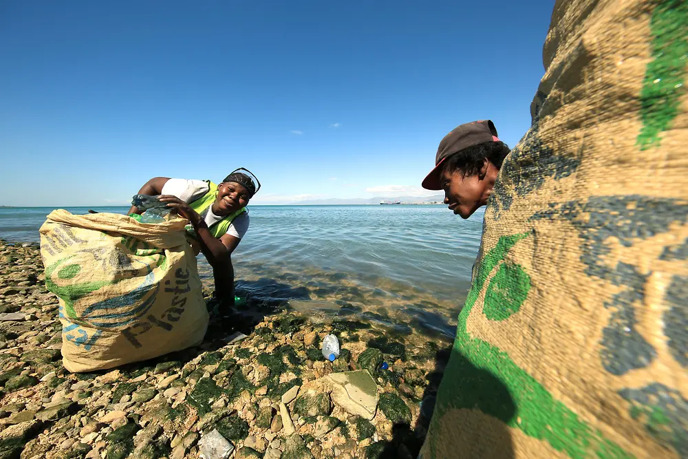 Proyecto de banco de plástico: 2 personas recogiendo plástico en una playa
