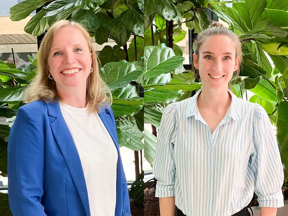 Dos Talent Acquisition Partners de pie frente a grandes plantas en un espacio de oficinas, compartiendo recomendaciones para una entrevista exitosa.