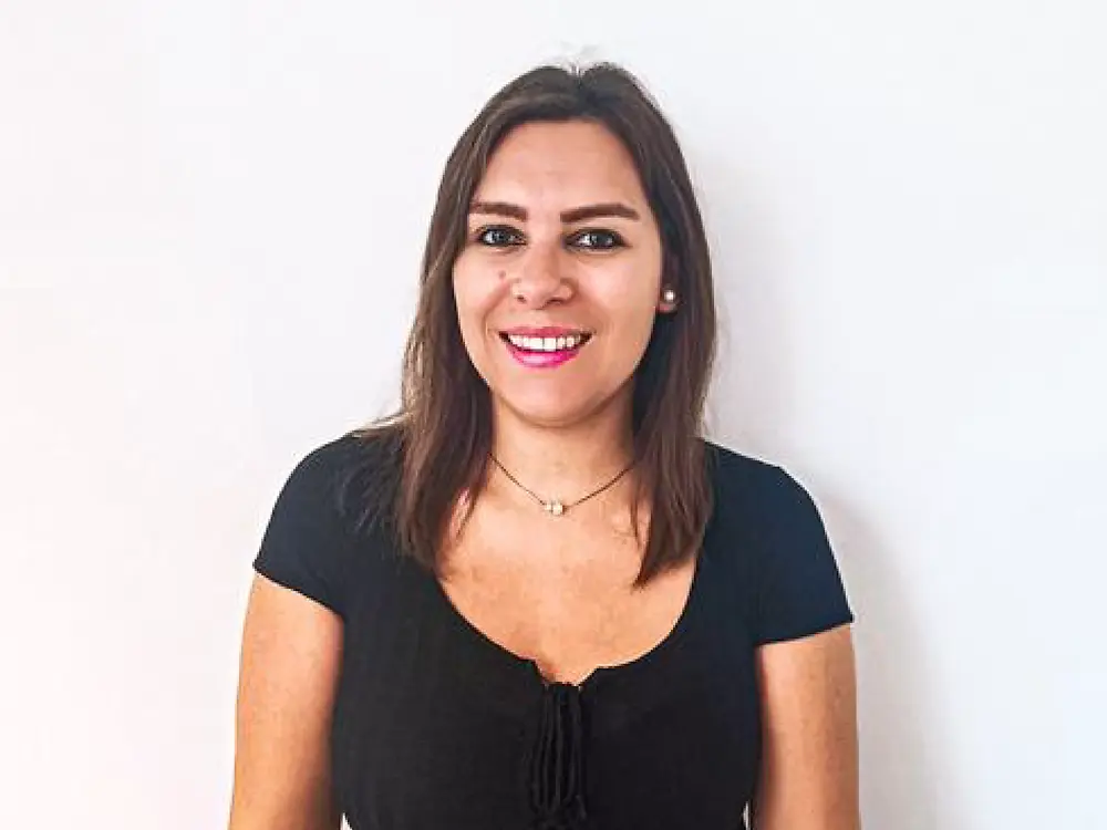 Una especialista en adquisición de talento, de pie frente a un fondo blanco, comparte recomendaciones para responder preguntas difíciles durante una entrevista.
