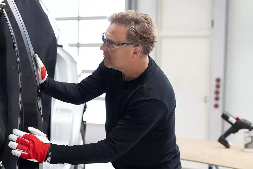 Técnico reparando o dando mantenimiento a la puerta de un vehículo en un taller automotriz.