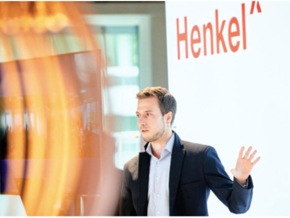 Empleados en frente de una pantalla con el nombre de Henkel en una presentación. 